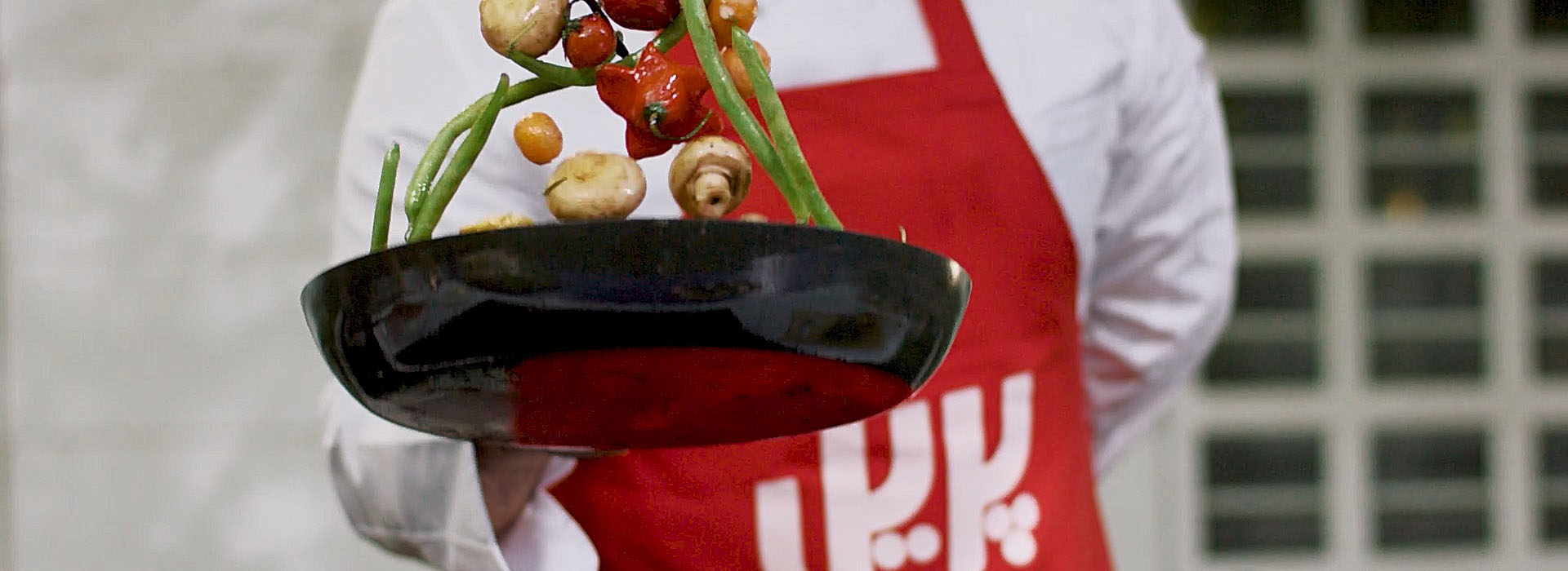 A chef influencer sautéing veggies in a red pril apron for the enjoy together campaign