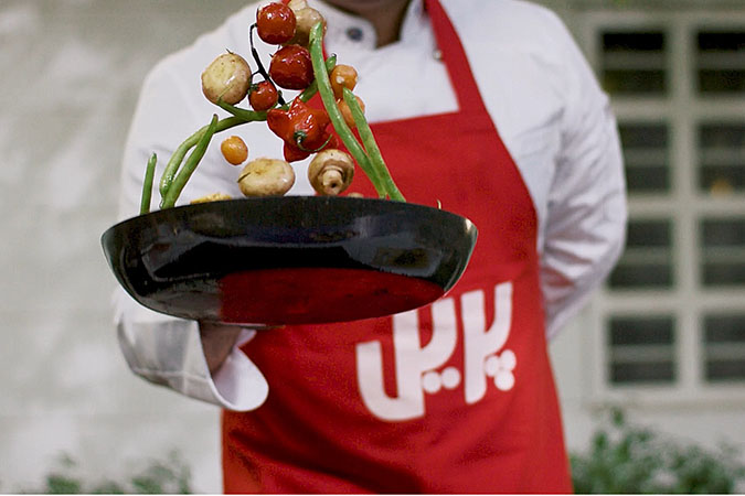 A chef sautéing veggies wearing a pril red apron